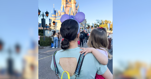 Woman standing holding her toddler at Disney World, wearing an open-back top revealing a spinal fusion scar.